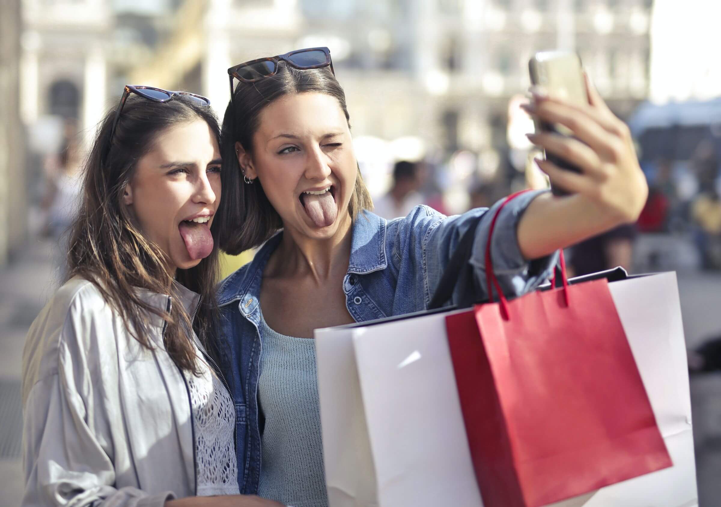 Cheerful young women with shopping bags taking selfie on street